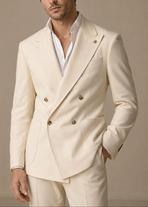 A man wearing a cream-colored double-breasted suit jacket with gold buttons over a white dress shirt, posed against a neutral beige background.